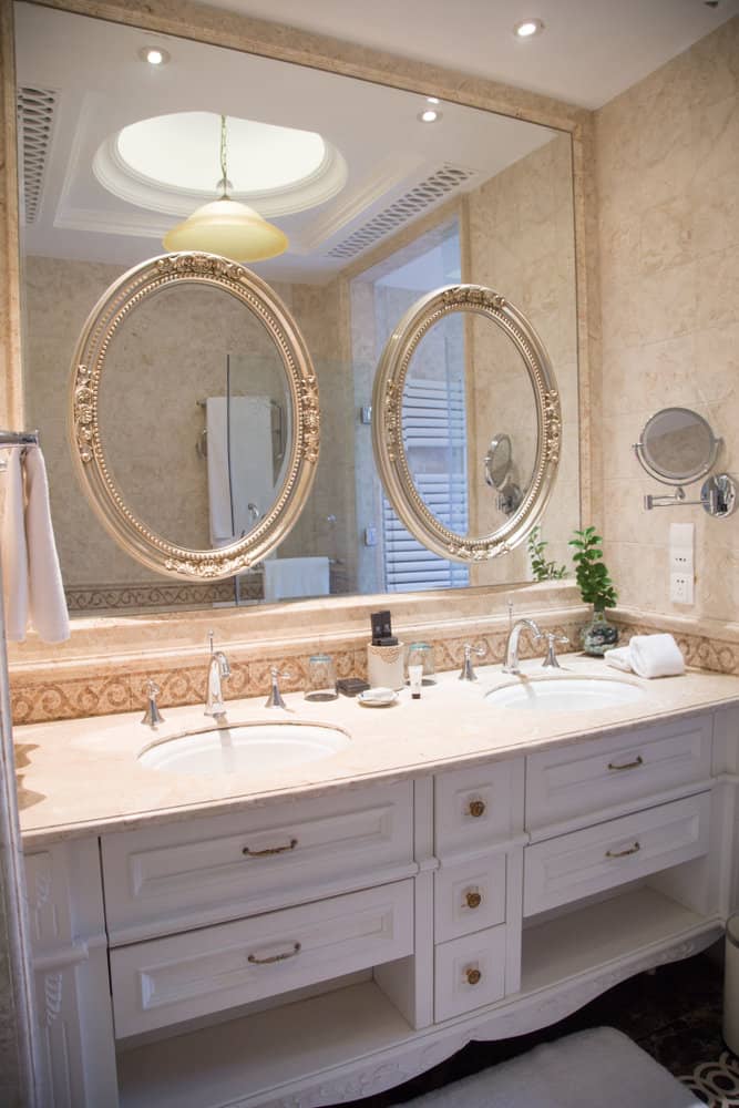 Elegant bathroom with dual sinks, marble countertop, and ornate round mirrors, towel and plant decor on the counter