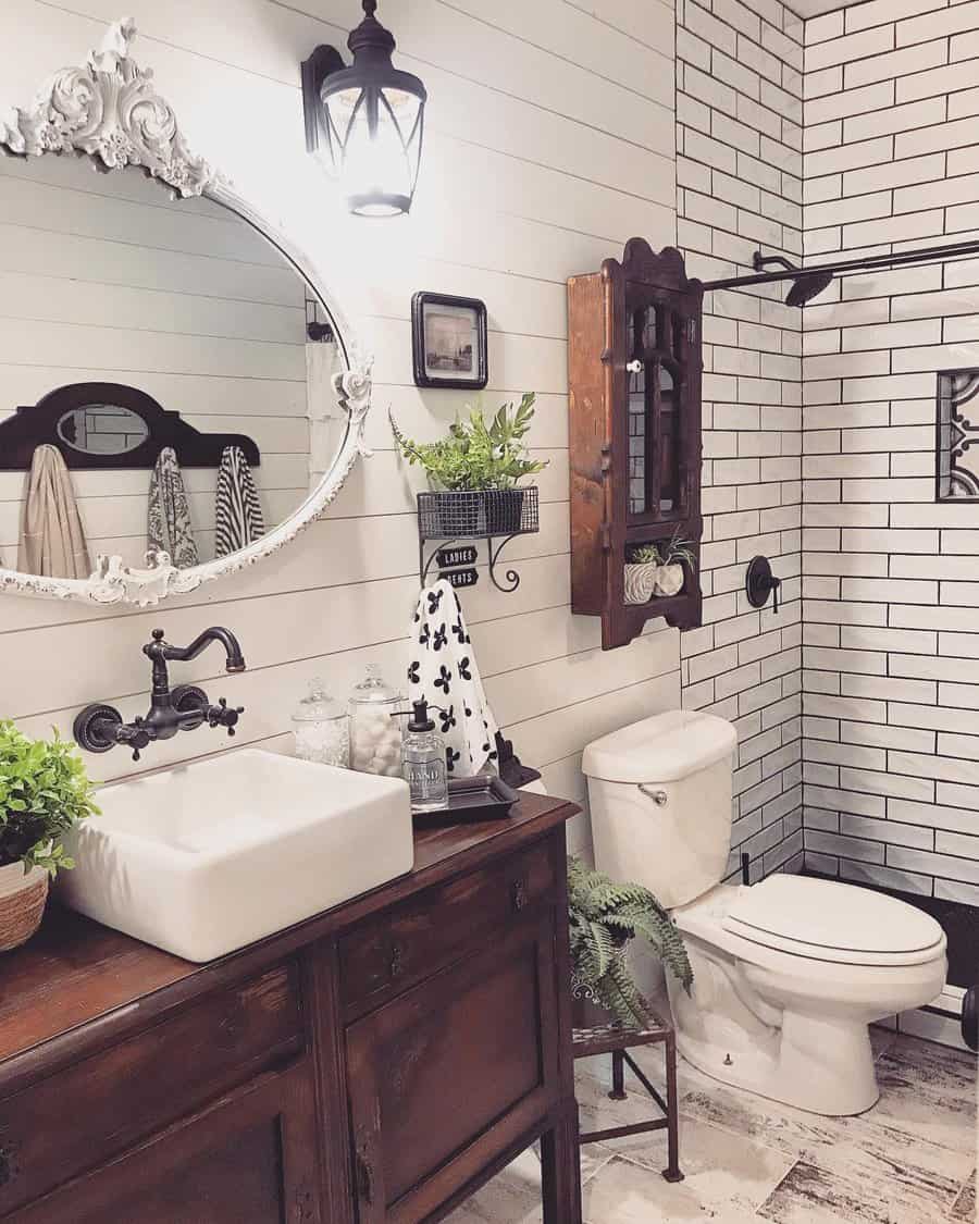 Rustic bathroom with a white sink on a wooden cabinet, round mirror, wall-mounted plants, and white subway tiles