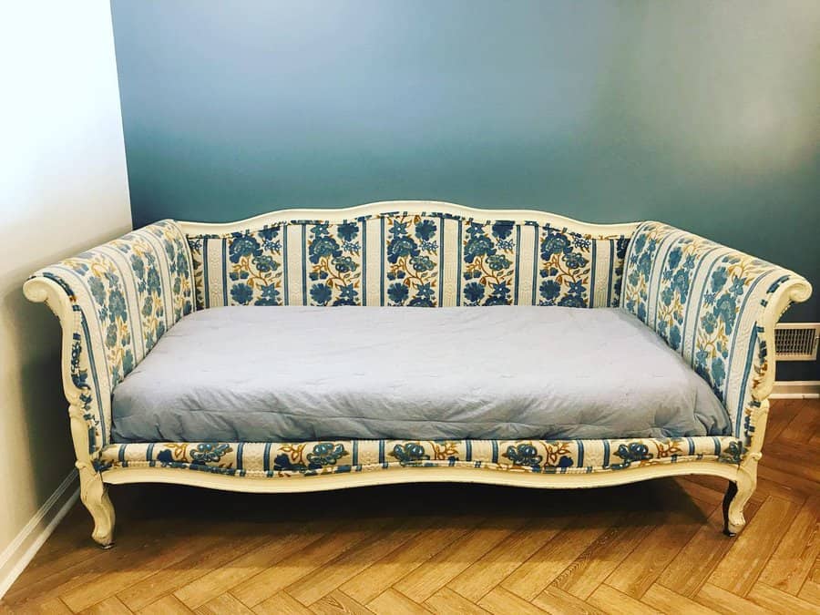 Vintage floral-patterned daybed with a blue cushion against a teal wall on a wooden herringbone floor