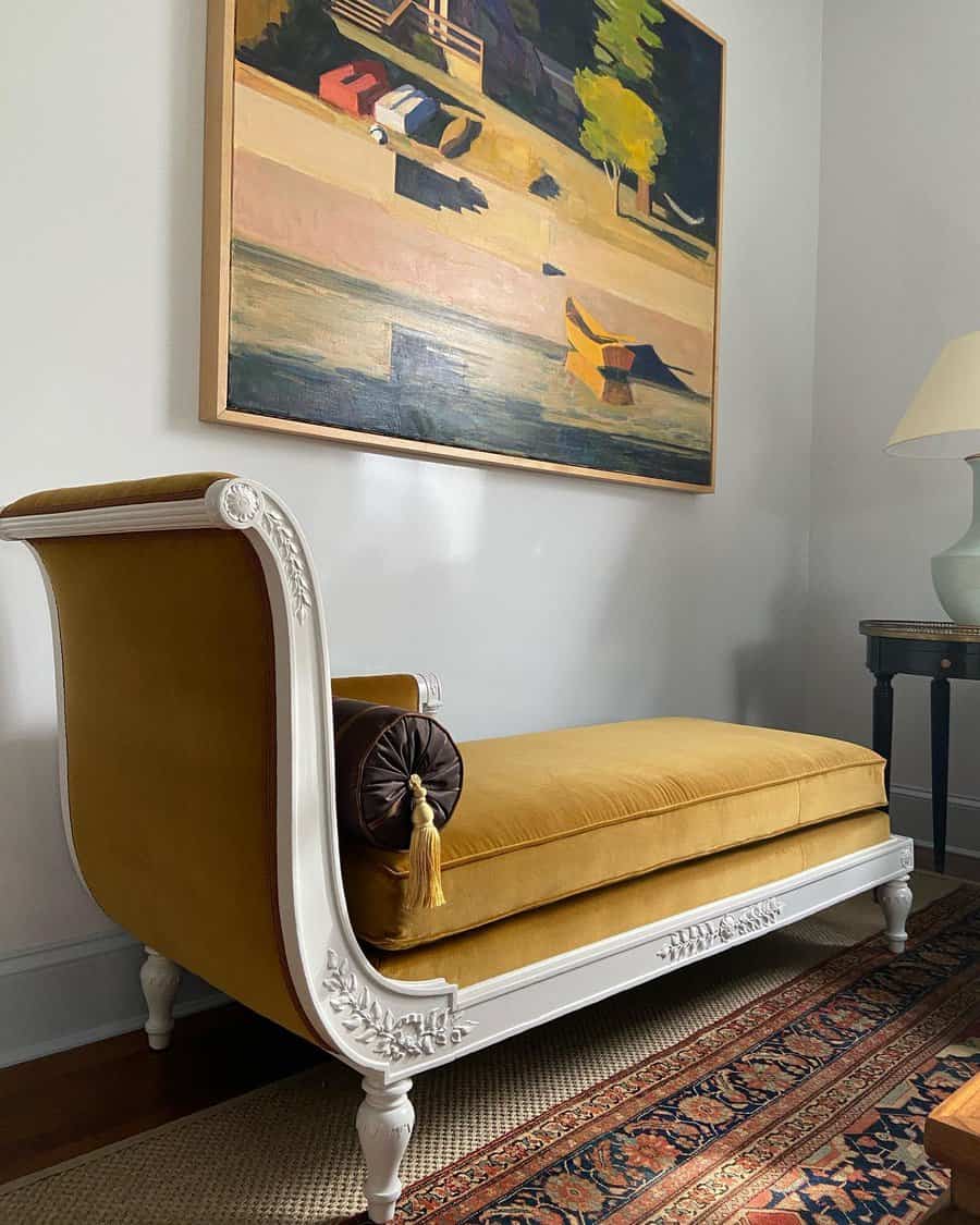 Elegant vintage-style daybed with mustard velvet upholstery, white carved wood details, and a classic bolster pillow, creating a luxurious seating area