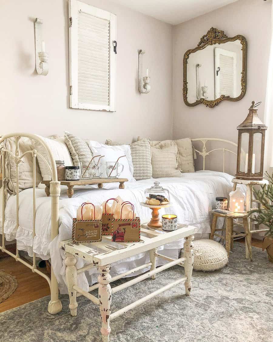 Vintage-style room with a white iron daybed, ornate mirror, distressed table with gift bags, lantern, candles, and a cozy, neutral palette