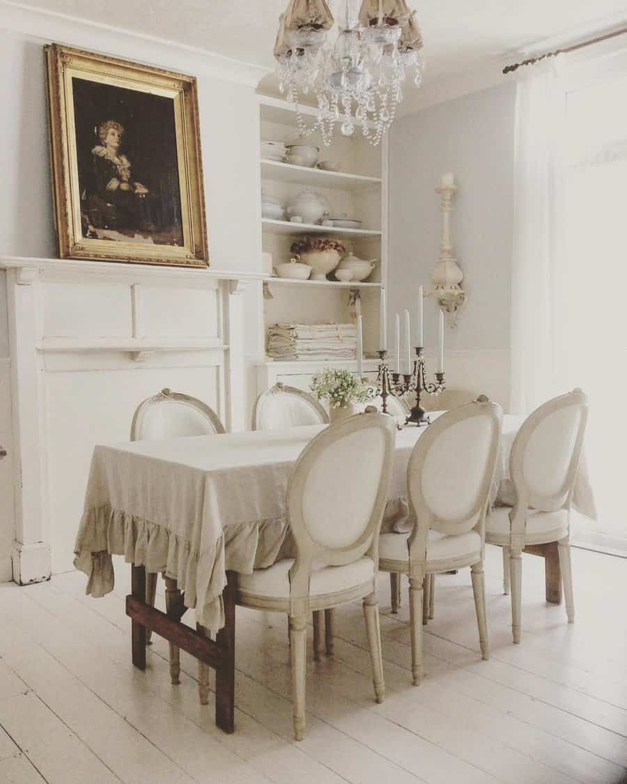 Rustic dining room with a chandelier, a portrait, a table with four chairs, and shelves with dishes, all in neutral tones