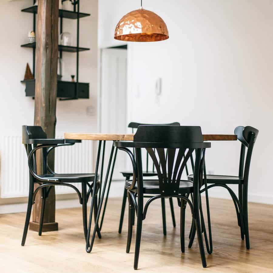 Dining area with a wooden table, four black chairs, a wooden beam, and a copper pendant light