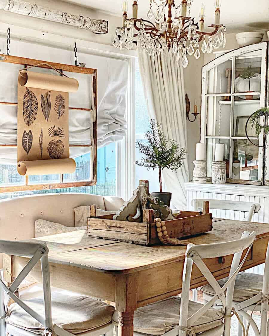 Rustic dining room with a wooden table, rustic chairs, a botanical scroll, and a small tree centerpiece, featuring vintage decor and chandelier