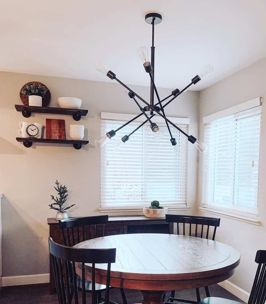 Dining room with a round wooden table, four chairs, a modern sputnik chandelier, and shelves with decor against white blinds