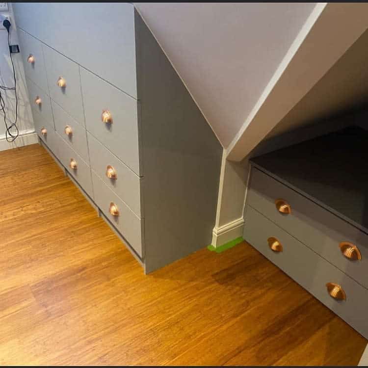 Custom-built attic storage drawers with sleek gray finish and copper handles, maximizing space under sloped ceilings with a stylish design.