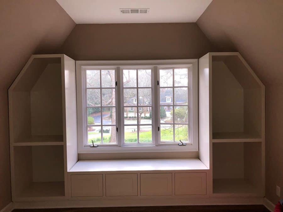 Custom-built attic window seat with built-in storage drawers and side bookshelves, creating a cozy and functional reading nook.