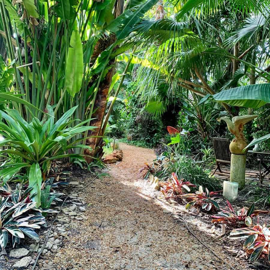 Lush tropical Florida garden with a winding gravel pathway, towering palms, vibrant foliage, and a cozy seating area for a serene jungle-like retreat