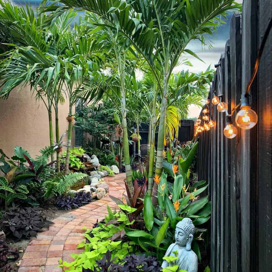 Serene Florida garden walkway with palm trees, tropical plants, string lights, a Buddha statue, and a peaceful water feature for a tranquil, Zen-inspired retreat