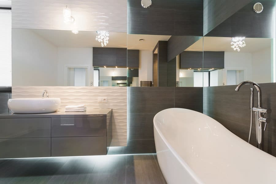 Modern bathroom with a freestanding tub, dark gray vanity with a vessel sink, large mirrors, and elegant pendant lights