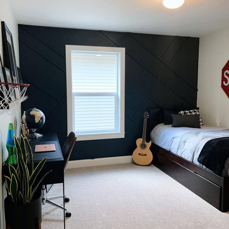 Minimalist bedroom with a black accent wall, single bed, guitar, desk with chair, globe, and a small basketball hoop