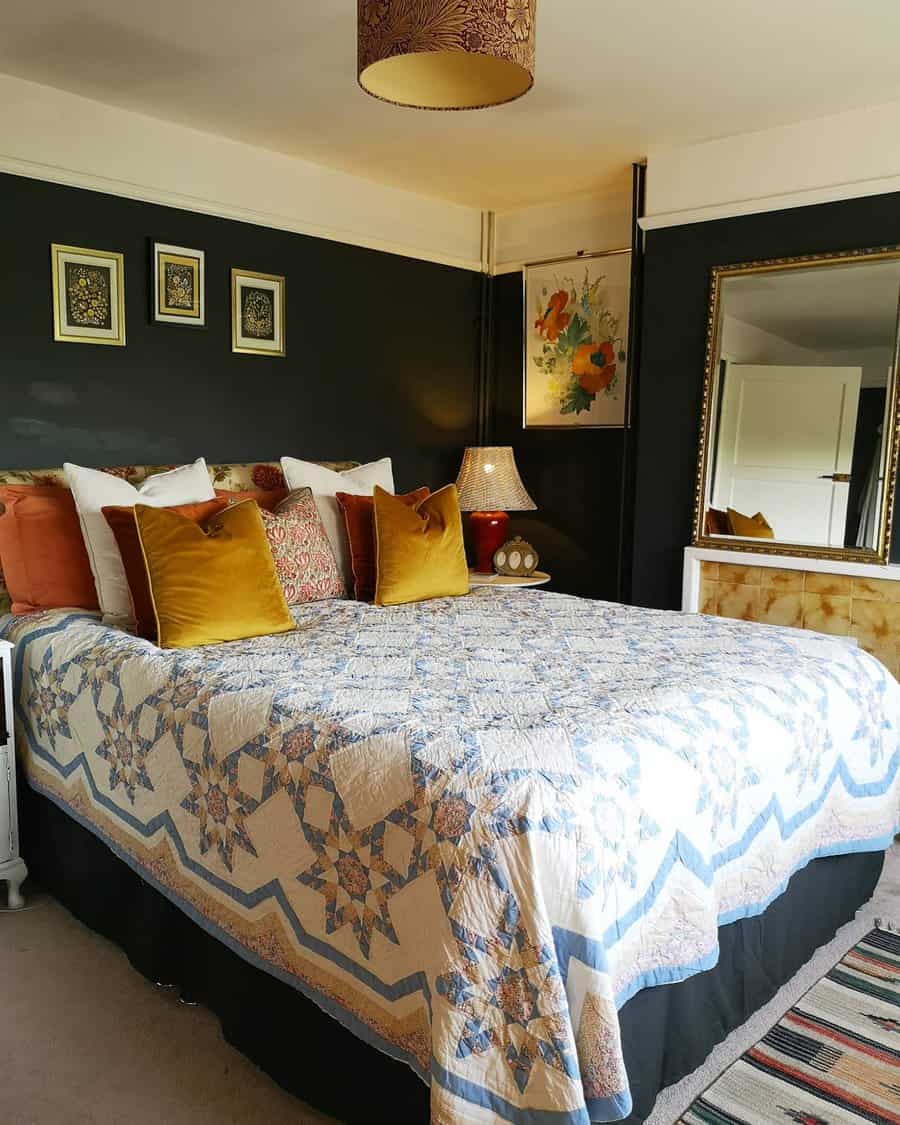 Cozy bedroom with a patterned quilt on the bed, decorative pillows, dark walls, a large mirror, and framed art on the walls