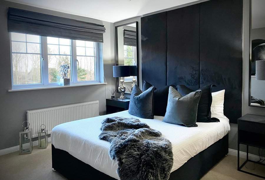 Chic black bedroom with a tall upholstered headboard, luxe velvet pillows, mirrored accents, and soft natural light from wide windows