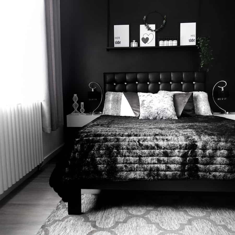 A monochrome bedroom with a black bed, pillows, and throw features decor that includes wall art, small plants, and a window with curtains