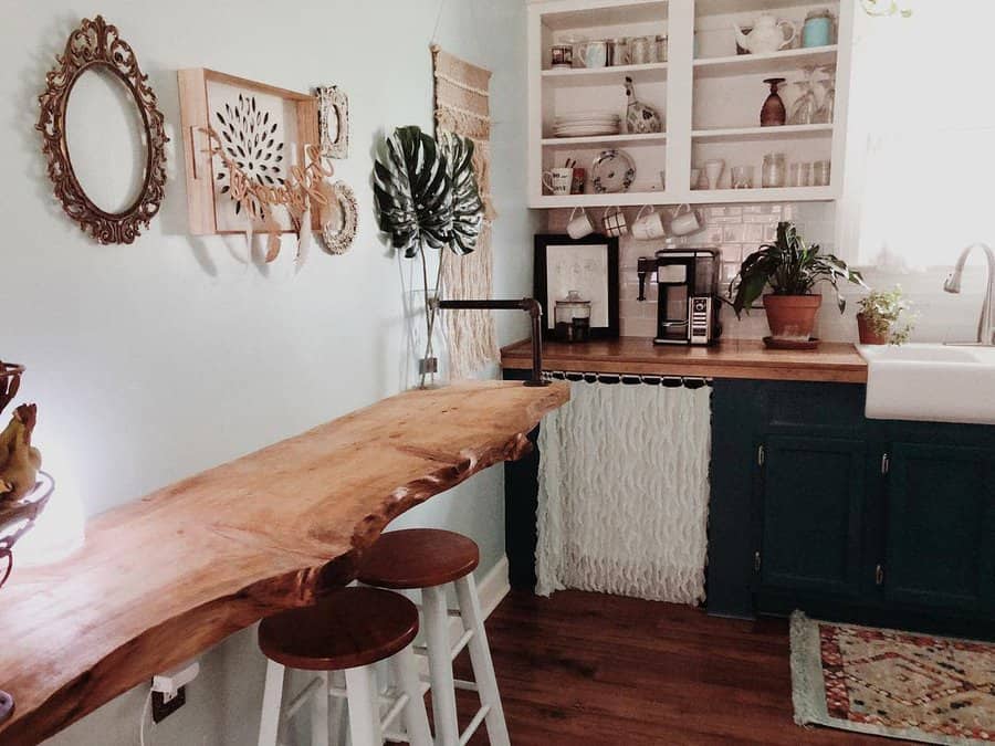 Boho-inspired kitchen with a rustic live-edge wooden wall breakfast bar, white barstools, open shelving, macrame accents, and warm earthy tones