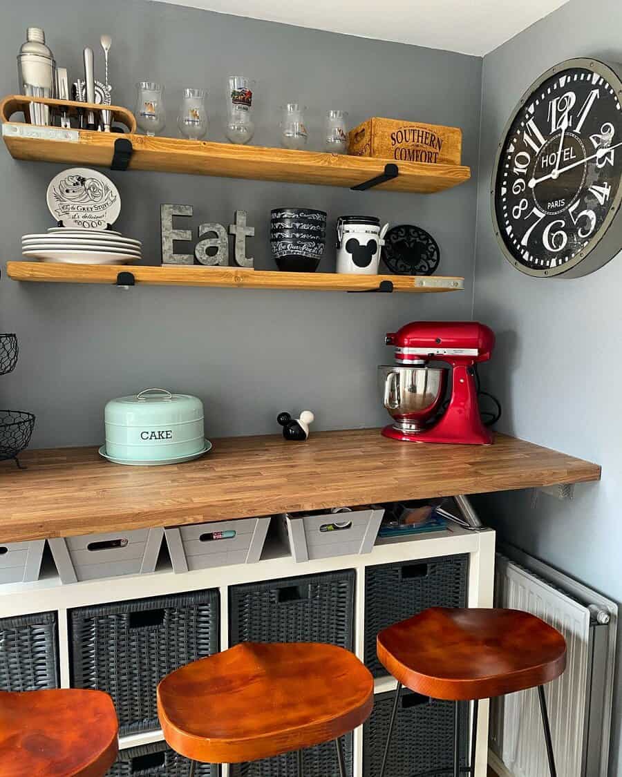 Rustic breakfast bar with a wooden countertop, open shelving, industrial-style barstools, wicker storage baskets, and a vintage wall clock for charm