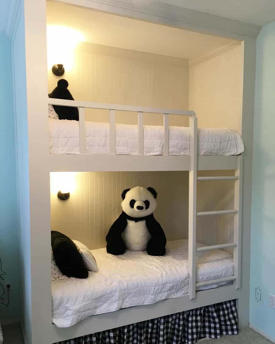 Bunk beds with white bedding, two black pillows, a large panda toy on the bottom bed, and two wall-mounted lights