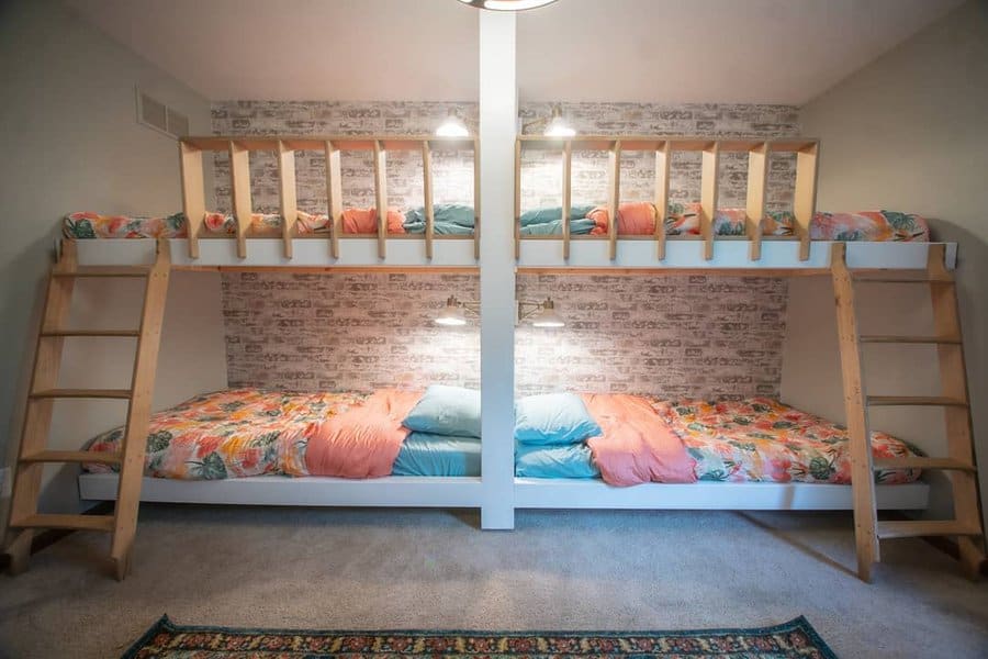 Cozy bedroom with two sets of bunk beds, wooden ladders, floral bedding, and a brick-patterned accent wall