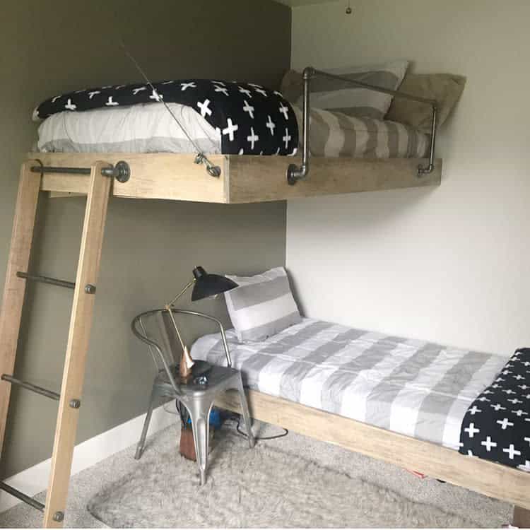 Bunk bed with a gray and white striped lower bed and black patterned upper bed, metal chair and lamp beside a wooden ladder