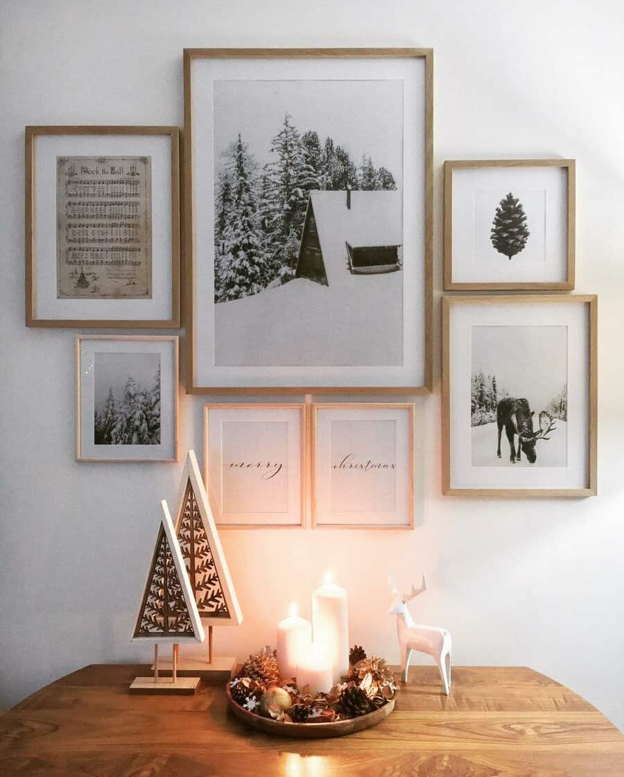 Framed winter-themed prints on wall, wooden table with candles and Christmas decor