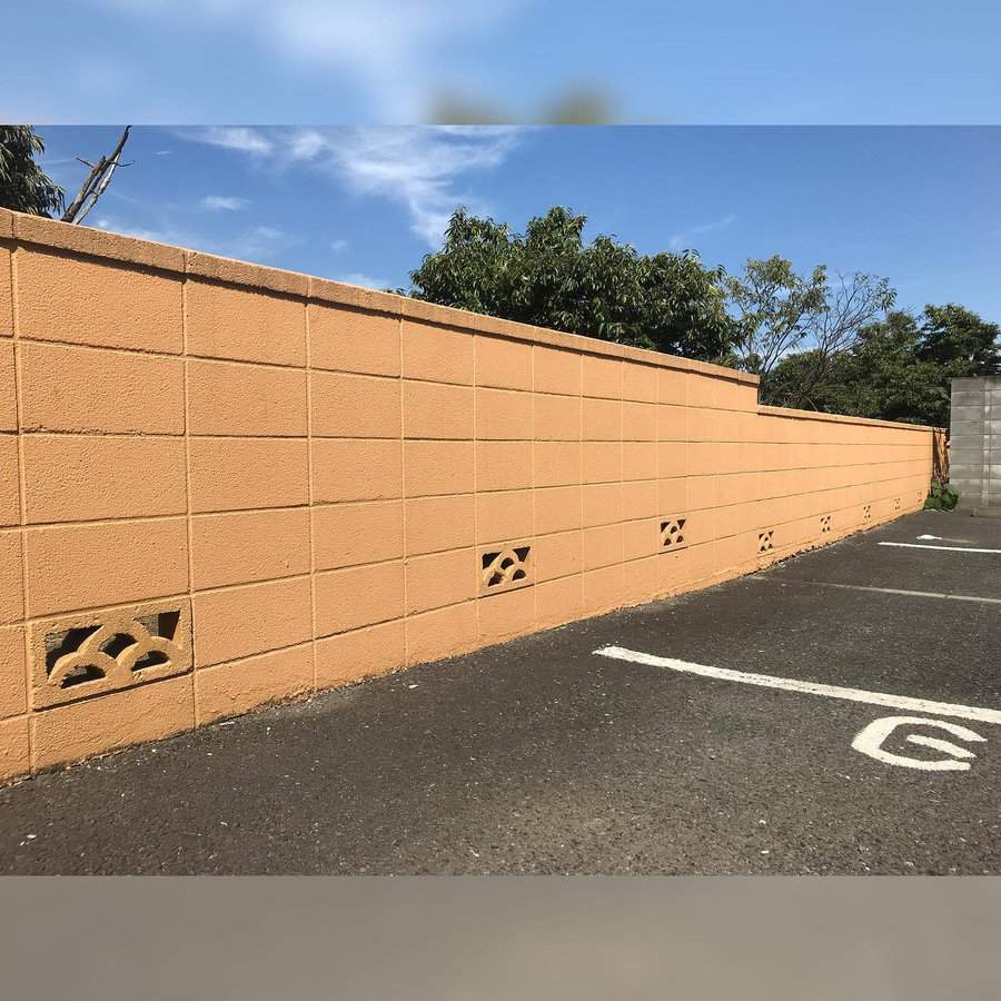 Tan concrete wall with patterned cutouts, next to empty parking spaces marked by white lines and letters