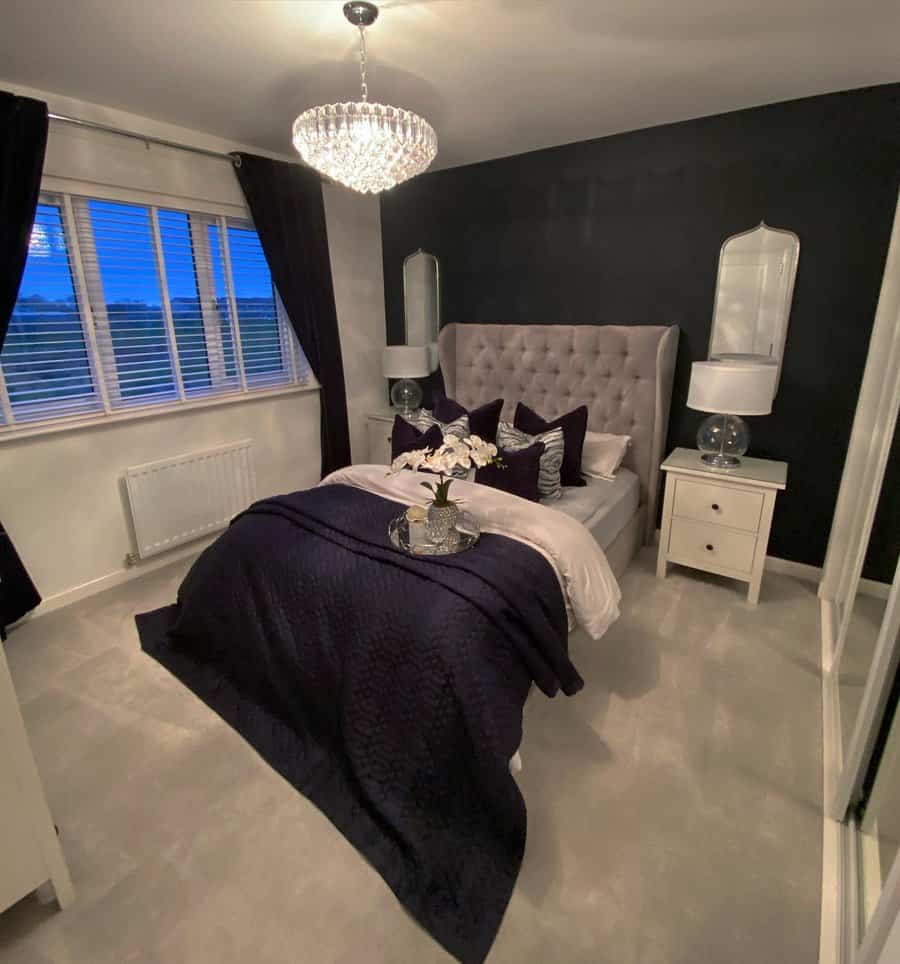 Master bedroom with a tufted headboard, dark bedding, white nightstands, and a chandelier; dark accent wall and large window with curtains