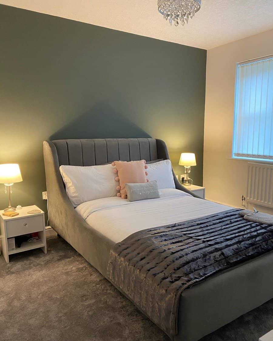 Cozy bedroom with a green accent wall, grey upholstered bed, white bedding, pink and grey pillows, bedside tables and lamps