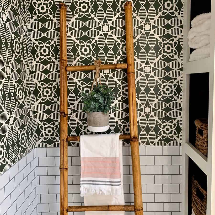 A stylish RV bathroom corner with a bamboo towel ladder, a hanging plant, and bold patterned wallpaper, paired with classic subway tiles for a chic and functional design.