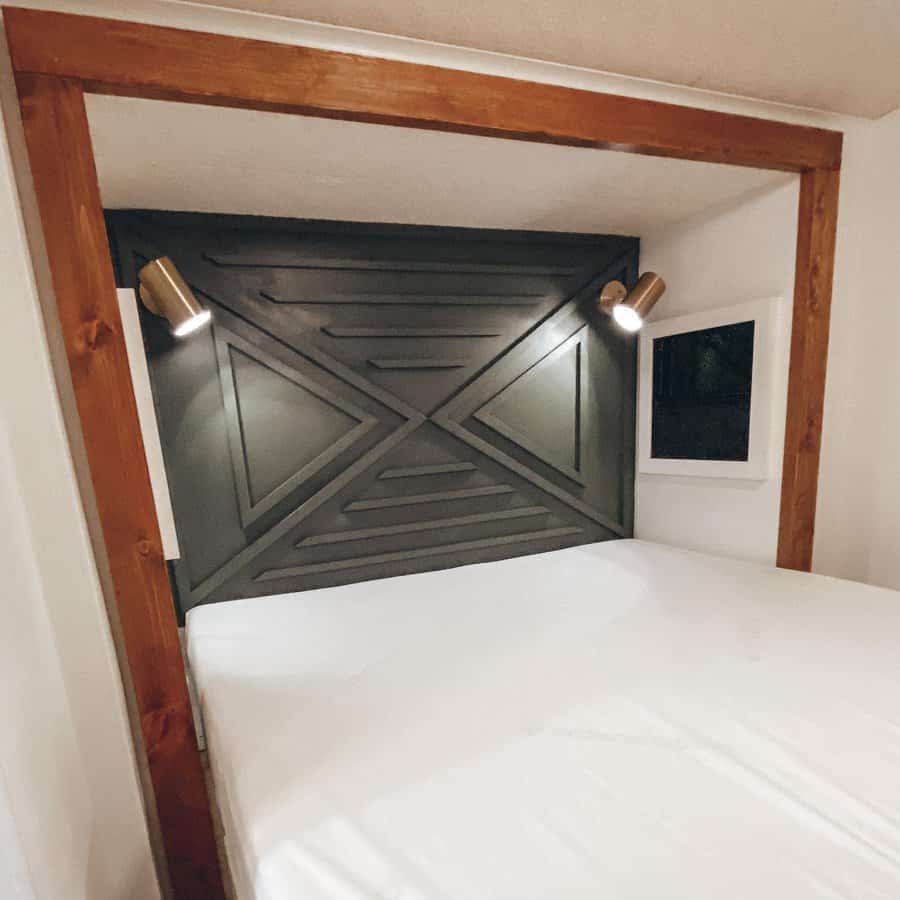 A rustic RV bedroom featuring a geometric headboard with accent lighting, creating a stylish and modern look.