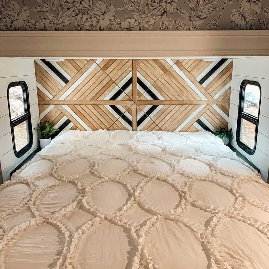 A stunning RV bedroom with a geometric wooden accent wall in natural tones, complemented by a textured white quilted bedspread and a peaceful atmosphere.