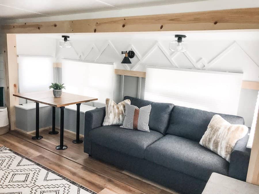 A modern RV living area featuring a gray sofa with cozy pillows, a sleek table, geometric wall decor, and a clean, stylish design.