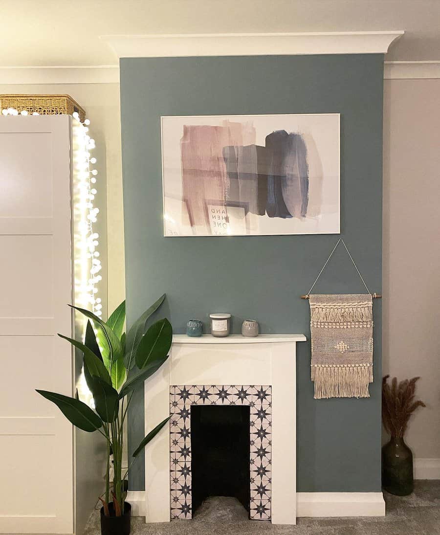 Stylish room with a teal accent wall, minimalistic art, potted plant, decorative fireplace, candles, and macramé wall hanging