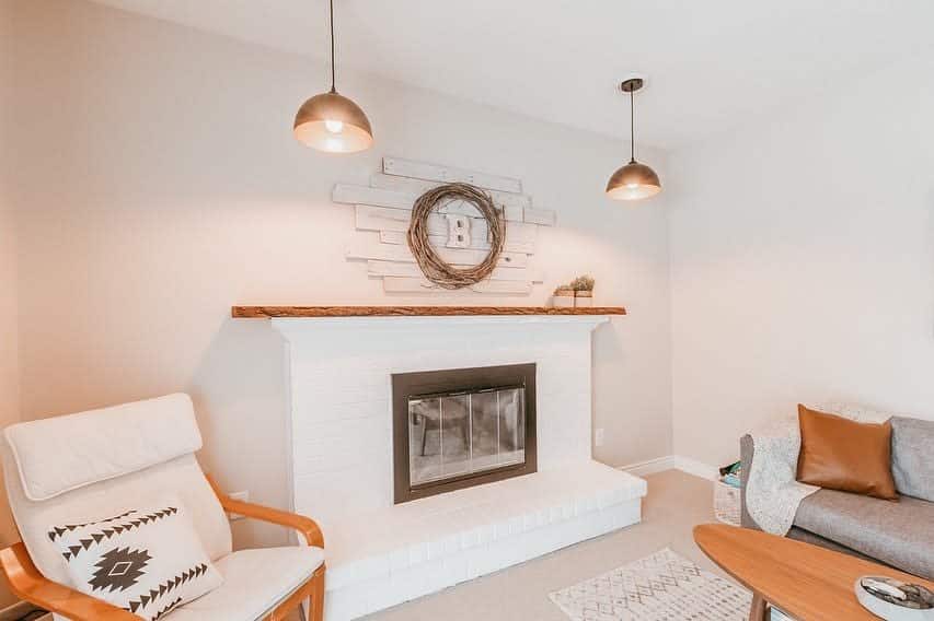 Cozy living room with a white brick fireplace, round mirror, two pendant lights, chair with patterned pillow, and a sofa with cushions