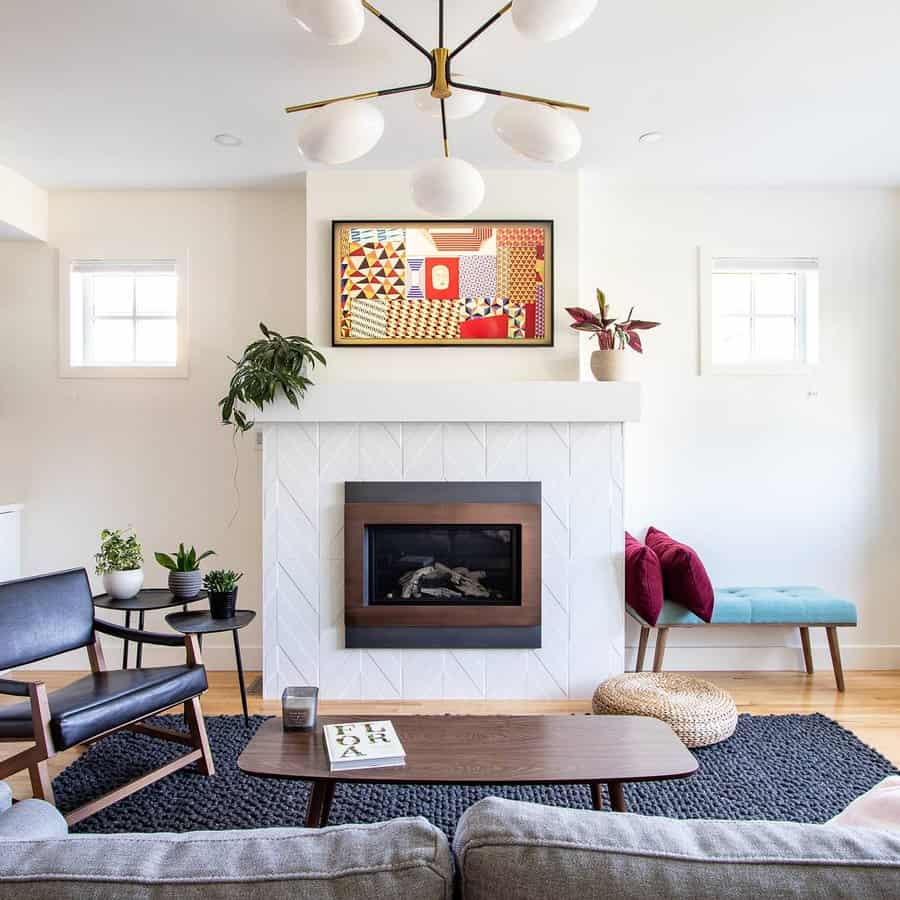 Modern living room with a geometric light fixture, artwork above a white fireplace, plants, and a mix of seating on a textured rug