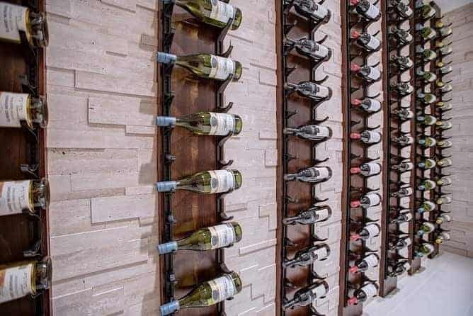 Wall-mounted wine rack displaying rows of wine bottles in an organized fashion against a light stone background