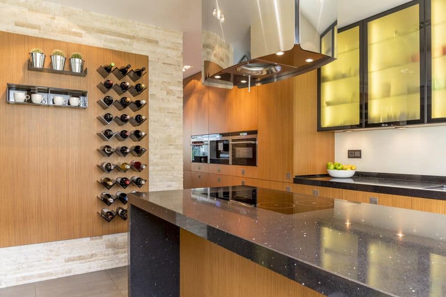 Modern kitchen with a sleek wall-mounted wine rack, warm wood cabinetry, black stone countertops, and illuminated glass cabinets