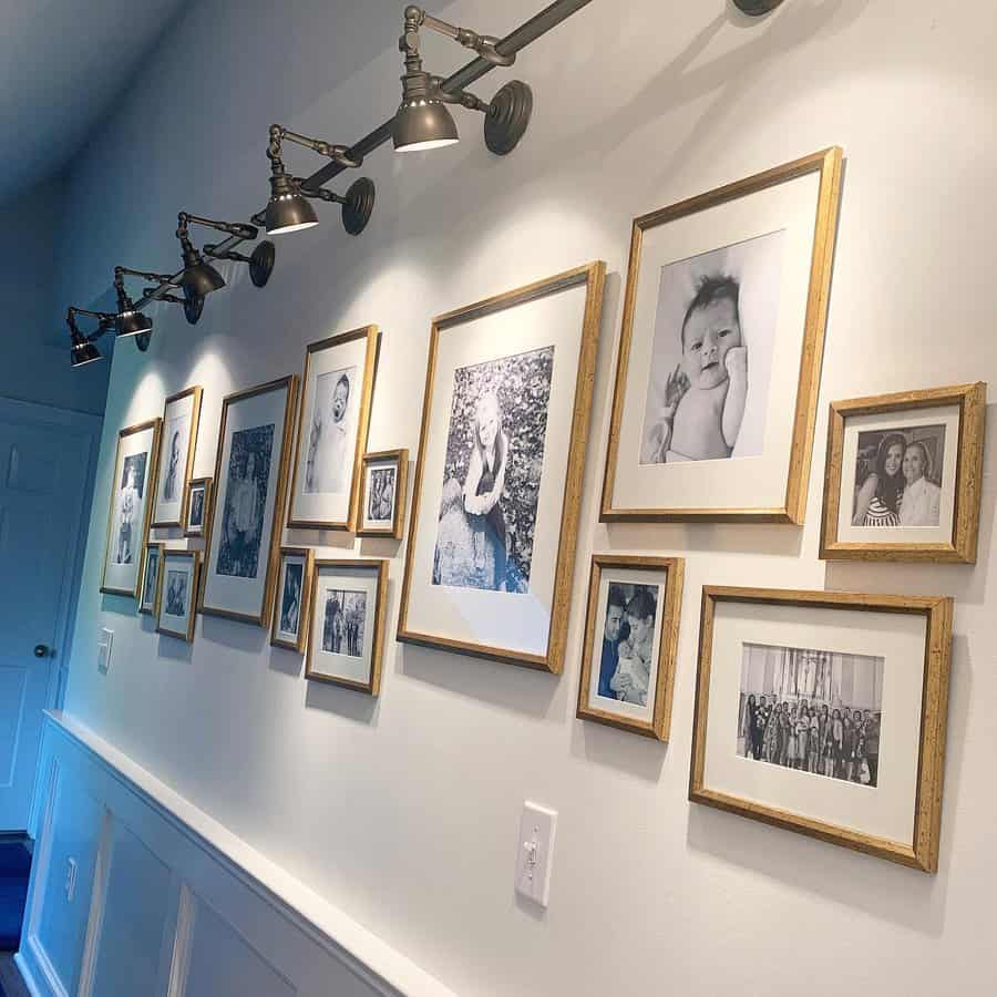 A hallway with framed family photos on the wall, lit by adjustable wall-mounted lamps