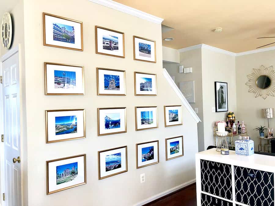 Wall with a grid of framed photographs, a staircase, and a white cabinet with decorative items in a well-lit room