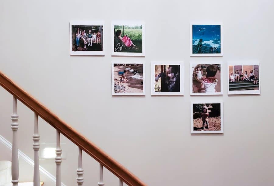 Photos arranged in a grid on a white wall above a staircase with a wooden handrail