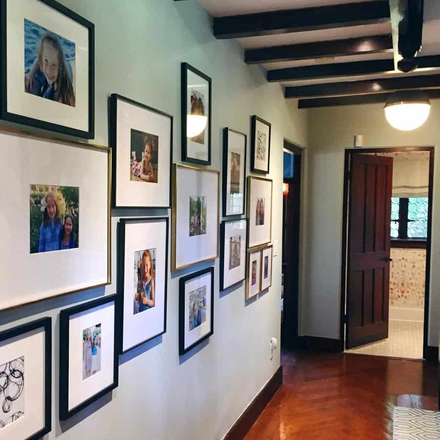 Hallway with framed photos and artwork on the wall, leading to a doorway with a glimpse of a bathroom