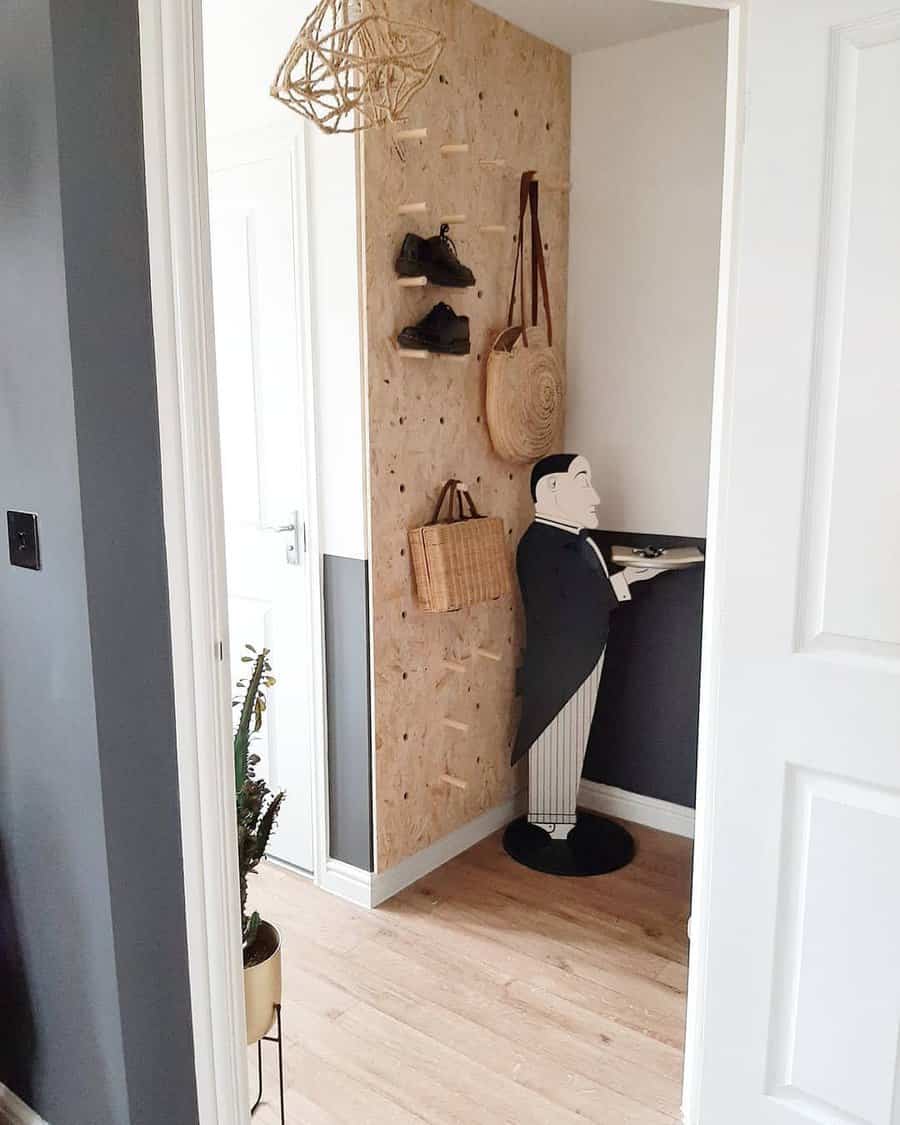 Corner shelf with shoes, bags, and a butler statue holding a tray; white walls, light wood floor, and dark accent wall with plants