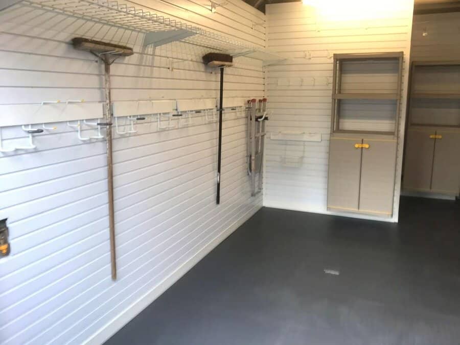 A neatly organized garage with wall-mounted storage hooks, shelves, and cabinets, maximizing space for tools, cleaning supplies, and equipment