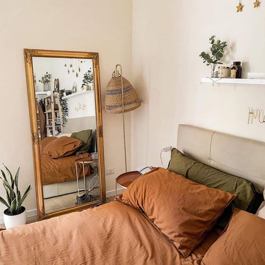 Cozy bedroom with earthy tones, featuring a large ornate mirror, a rattan lamp, plants, and a shelf with decor items above the bed