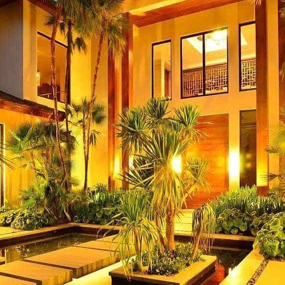 Tropical courtyard with tall plants, warm lighting, and reflecting water pool in a modern building setting at night