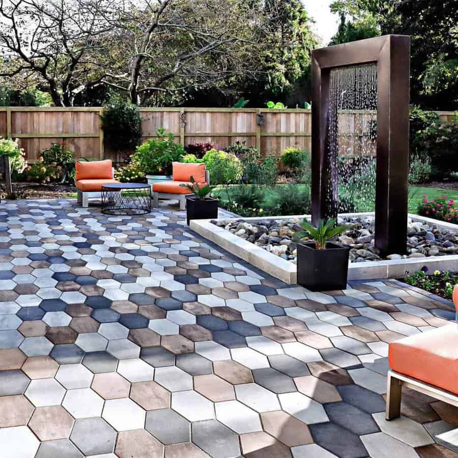 Backyard patio with hexagonal tiles, a modern water fountain, orange seating, and lush greenery