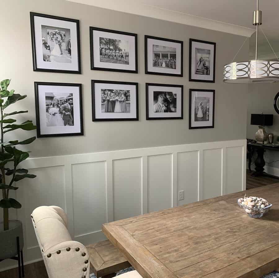 Dining room with a wooden table, beige chairs, framed black-and-white photos on the wall, a tall plant, and a modern light fixture