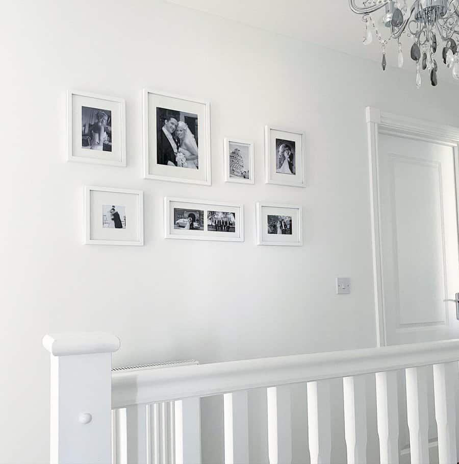 A white hallway with several black-and-white photos in white frames arranged on the wall above a staircase railing