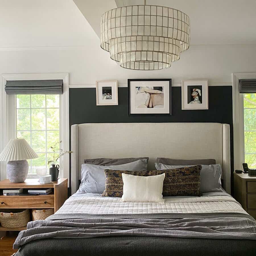 Cozy black and white bedroom with a large upholstered headboard, layered bedding, modern art, and soft natural light