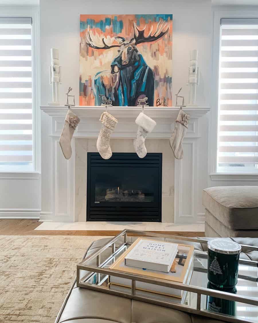 A modern white fireplace with stockings hung on the mantel, framed by a vibrant moose painting above and a sleek gas fire below, creating a cozy and festive ambiance