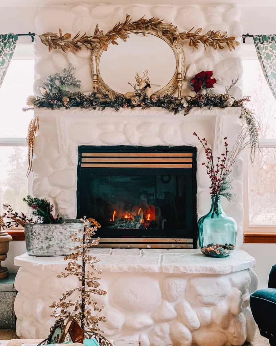 A rustic stone fireplace with a whitewashed finish, adorned with a golden mirror, festive garland, and seasonal decor, creating a cozy and inviting atmosphere